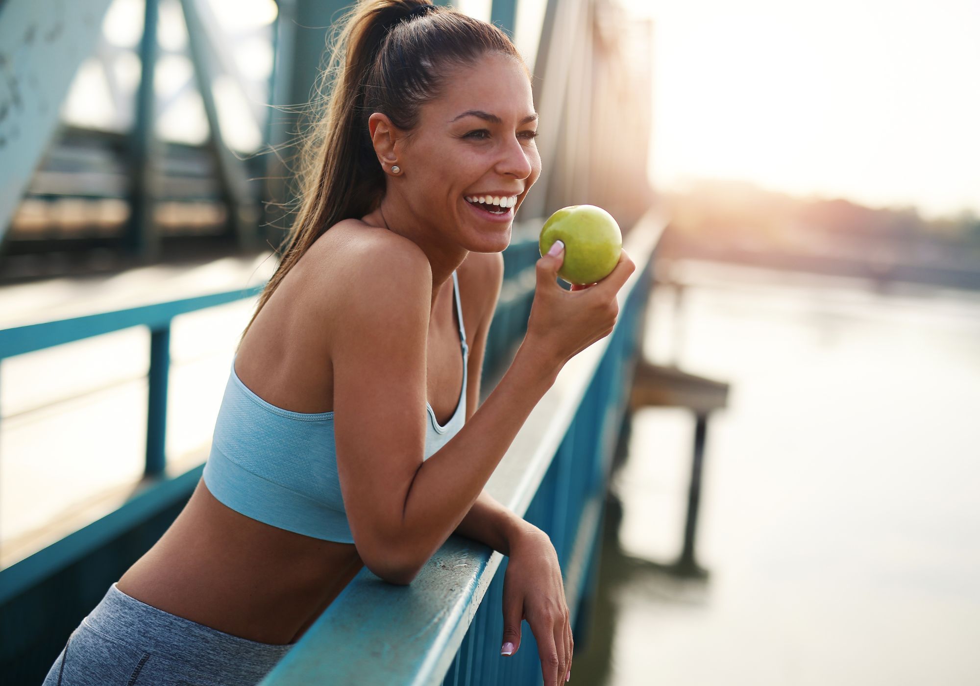 woman standing on a bridge with an apple, post workout